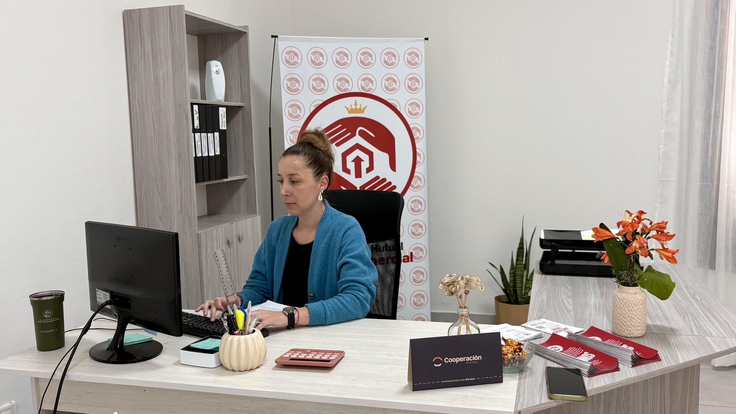 Oficina de atención de Mutual AFUCO: una colaboradora trabaja en su escritorio frente al banner con el isotipo de la Mutual.